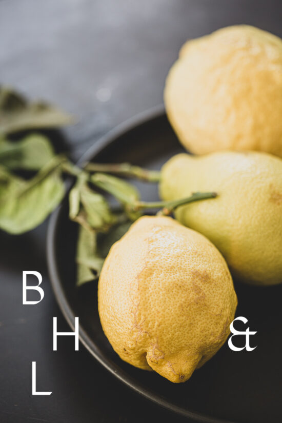 Food photography of lemons and lemon leaves on a black plate set on a black table
