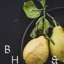 Food photography of lemons and lemon leaves on a black plate set on a black table