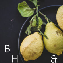 Food photography of lemons and lemon leaves on a black plate set on a black table