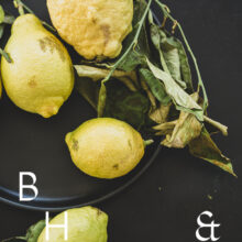 Food photography of lemons and lemon leaves on a black plate set on a black table