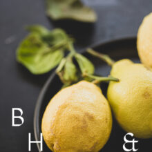 Food photography of lemons and lemon leaves on a black plate set on a black table