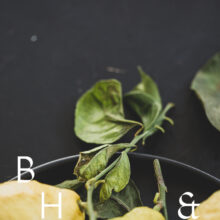 Food photography of lemons and lemon leaves on a black plate set on a black table