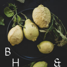 Food photography of lemons and lemon leaves on a black plate set on a black table