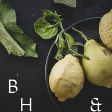 Food photography of lemons and lemon leaves on a black plate set on a black table