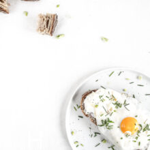Clean food photography with a sandwich and a sunny side up on a white plate and some bread