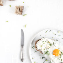 Clean food photography with a sandwich and a sunny side up on a white plate with a knife and some bread