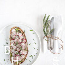 Clean food photography with a sandwich topped with radish on a white plate silverware and deco