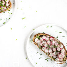 Clean food photography with a sandwich topped with radish on a white plate a silverware