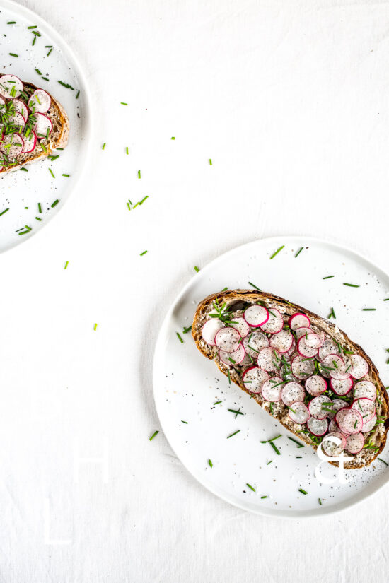 Clean food photography with a sandwich topped with radish on a white plate a silverware
