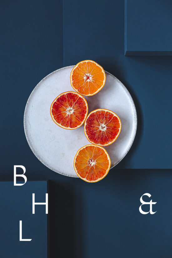 Food photography of Oranges cut half open on a white plate on blue ground