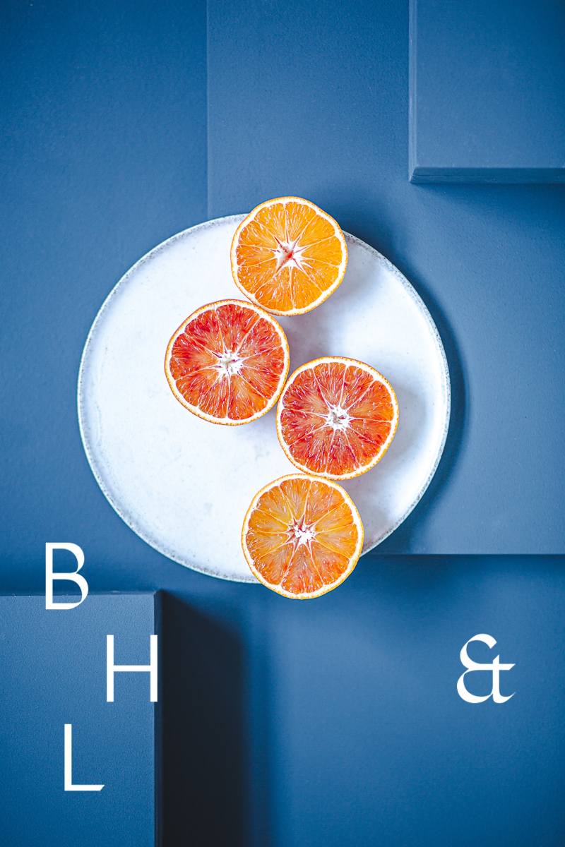 Food photography of Oranges cut half open on a white plate on blue ground