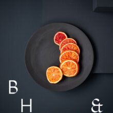 Food photography of blood-orange-cut in slices on a black ceramic plate on a dark grey ground