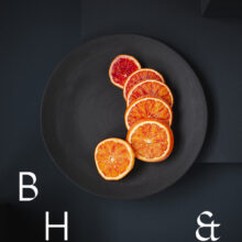 Food photography of blood-orange-cut in slices on a black ceramic plate on a dark grey ground