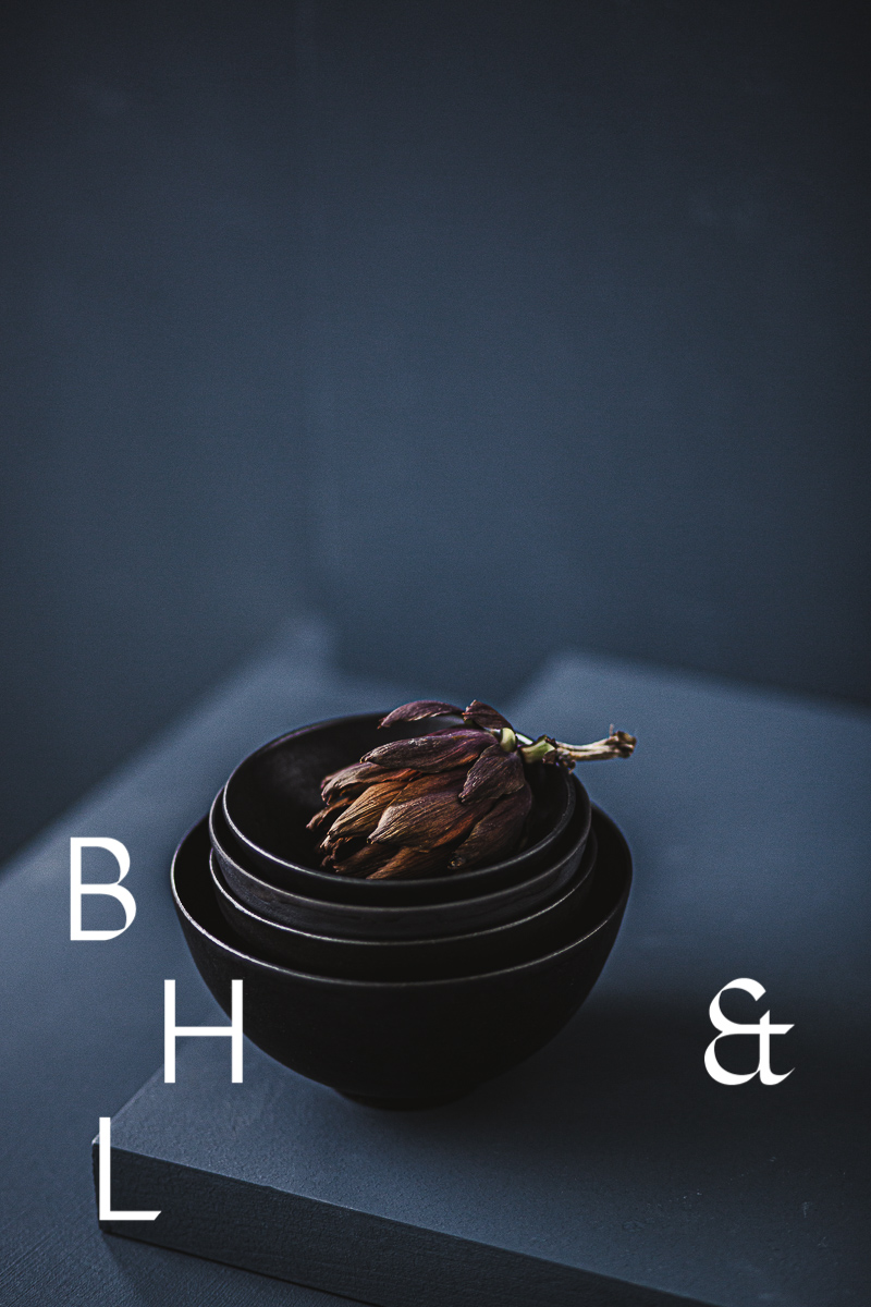 Food photography of artichoke in black ceramic bowels on a grey ground